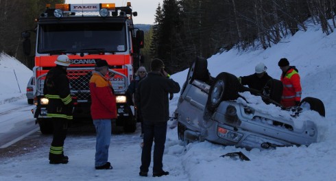 Bil på taket i snöigt dike med bärgare på vägen